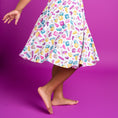 Load image into Gallery viewer, A child wearing the Block Party (Purple) Short Sleeve Big Kid Twirl Dress by Big Dreams Little Jammies, featuring fun cartoon bandage prints, stands barefoot on a purple background. The bamboo fabric is hypoallergenic and soft for sensitive skin.