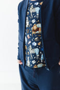 Load image into Gallery viewer, A person wearing the Jammie Session Up Zoo Late Solid Kids' Jacket (runs small, please size up), navy pants with hands in pockets, and an animal-themed shirt with zebras, lions, dogs, and space motifs.