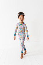 A young child models the Jammie Session Whispering Wildflowers Long Sleeve PJ's with a matching headband, walking barefoot on a white floor against a plain white background.