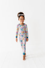 A young child wearing Jammie Session's Whispering Wildflowers Long Sleeve PJ's stands barefoot on a white floor against a plain white background.