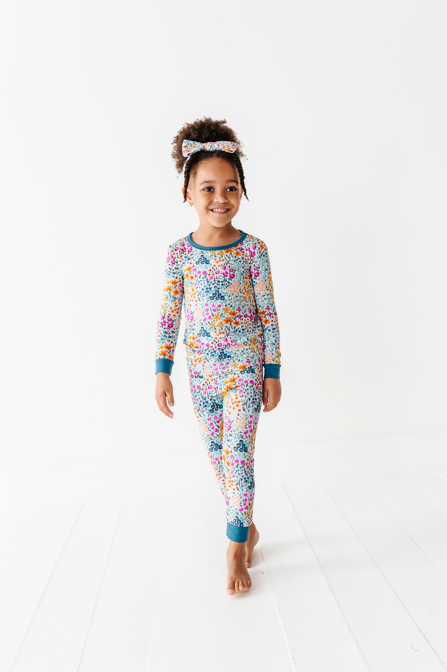 A young child wearing Jammie Session's Whispering Wildflowers Long Sleeve PJ's stands barefoot on a white floor against a plain white background.