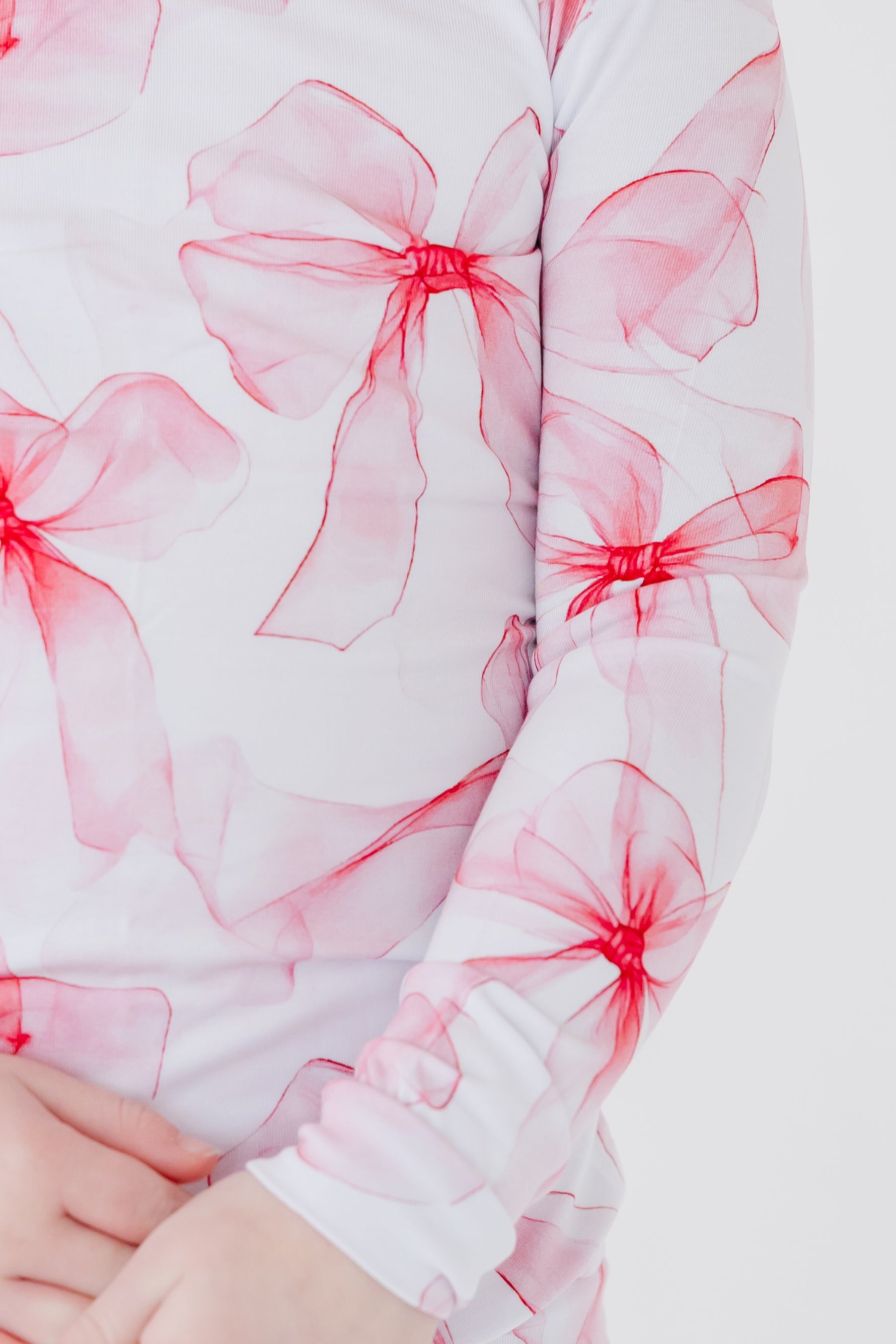 A close-up of a child in Jammie Session's Pretty in Bows Long Sleeve PJ's—white kids' bamboo pajamas with a playful pink and red bow print.