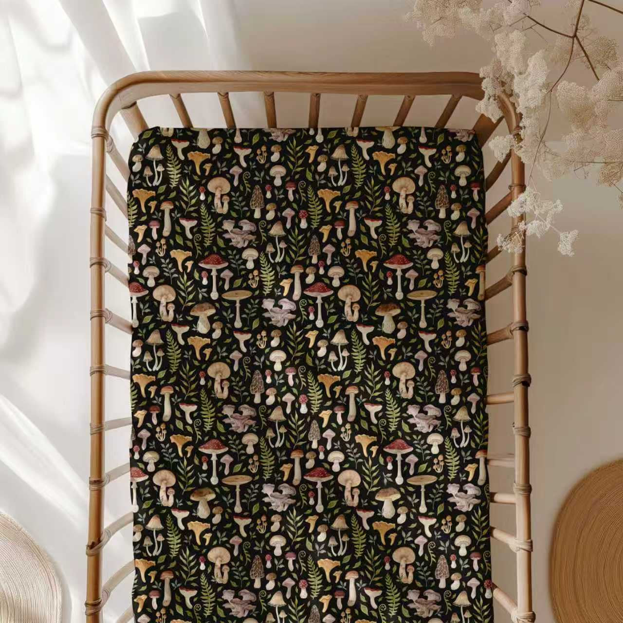 The Jammie Session Mystic Mushrooms Crib Sheet offers soft, hypoallergenic baby bedding with a colorful mushroom and botanical print, shown here in a wooden crib with a dark blanket and dried flowers in a softly lit room.