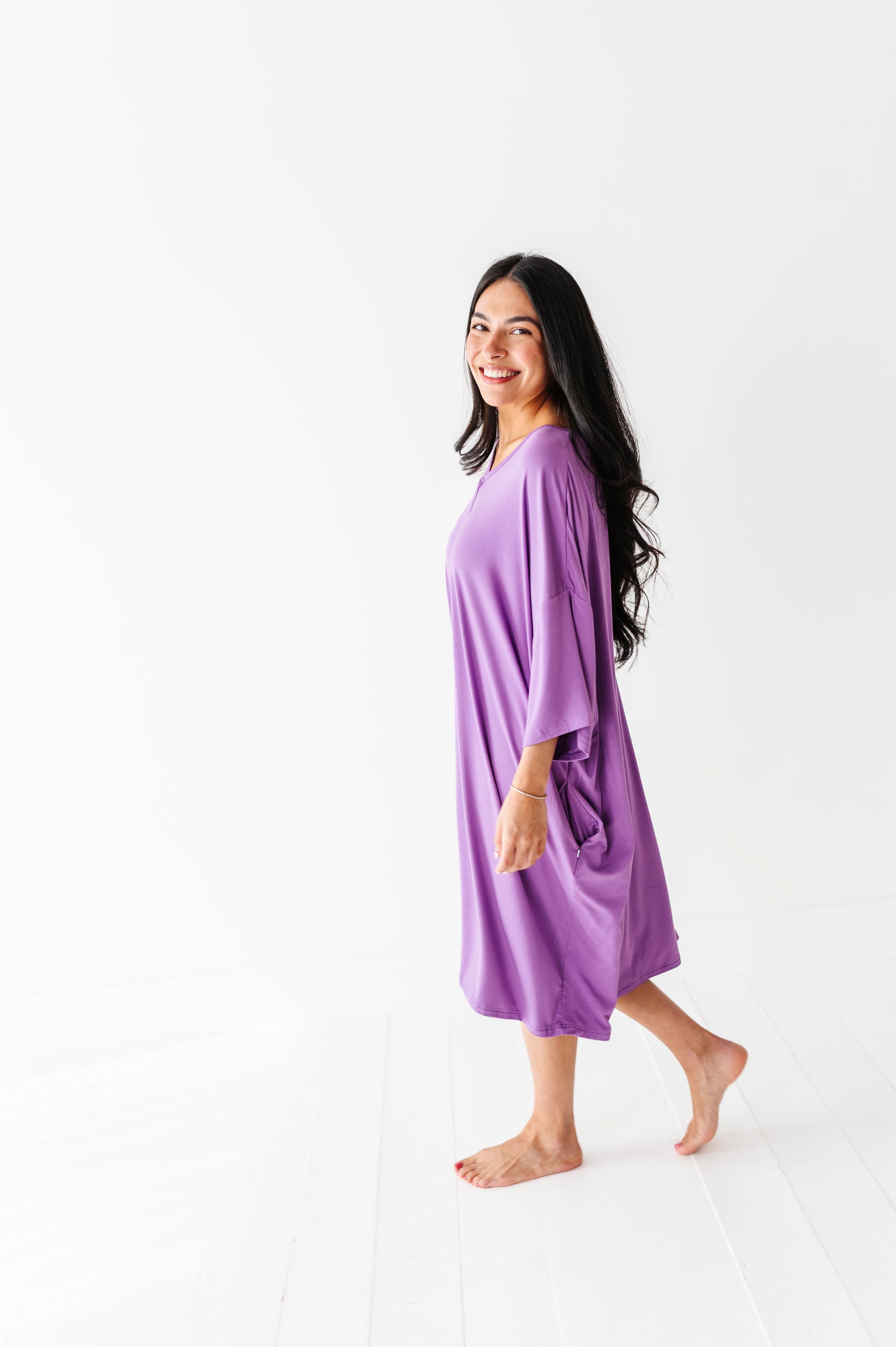 A woman stands barefoot on a white floor, smiling at the camera in the Jammie Session Block Party Solid Women's Muumuu Lounge Tee (ONE SIZE FITS XS - XXL), set against a plain white background.