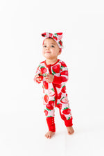 A toddler stands on a white surface, wearing the Jammie Session Berry Sweet (Strawberry) Romper with a matching headband, looking slightly upward and holding a small object in both hands.