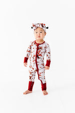 A toddler wears the Jammie Session Dreaming with Dragons Romper, a white and red bamboo pajama set with dragon print and matching headwrap, standing barefoot against a plain white background.