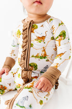A baby in the Jammie Session "Oh Bother, It's Bedtime Ruffle Romper"—a white bamboo long sleeve romper with animal and tree prints, brown ruffle trim, and cuffs—sits against a white background.