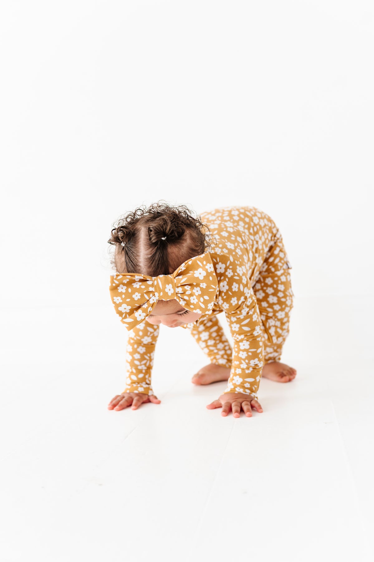 A baby wears the Jammie Session Honey Blooms Romper with a matching headband while bent over on hands and feet against a white background.