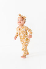A toddler wearing the Jammie Session Honey Blooms Romper and matching headband stands barefoot on a white background.