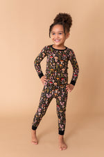 A young child smiles barefoot with hands on hips, wearing Jammie Session’s Mystic Mushrooms Long Sleeve PJ's—black bamboo pajamas featuring colorful mushroom patterns—combining comfort and style for fun at bedtime.