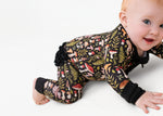 A baby crawls on a white surface in the adorable Mystic Mushrooms Ruffle Romper by Jammie Session, featuring a long-sleeve design with a colorful mushroom and foliage pattern.