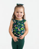 A young child with long brown hair wears the Jammie Session Bundle of Koi Bloomy Crop Set—featuring a matching floral top, hair bow, and dark green pants—standing and smiling against a plain white background.