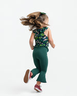 A young girl in the Jammie Session's Bundle of Koi Bloomy Crop Set is running and turning away from the camera on a white background, her light brown hair tied back as she moves mid-motion.