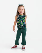 A young girl smiles in the Jammie Session Bundle of Koi Bloomy Crop Set—featuring a sleeveless floral top and green flared pants—paired with red sneakers and a coordinating hair bow against a plain white background.