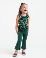 A young child smiles in the Jammie Session Bundle of Koi Bloomy Crop Set, featuring a green floral sleeveless top and matching pants, paired with red sneakers and a green hair tie, against a plain white background.