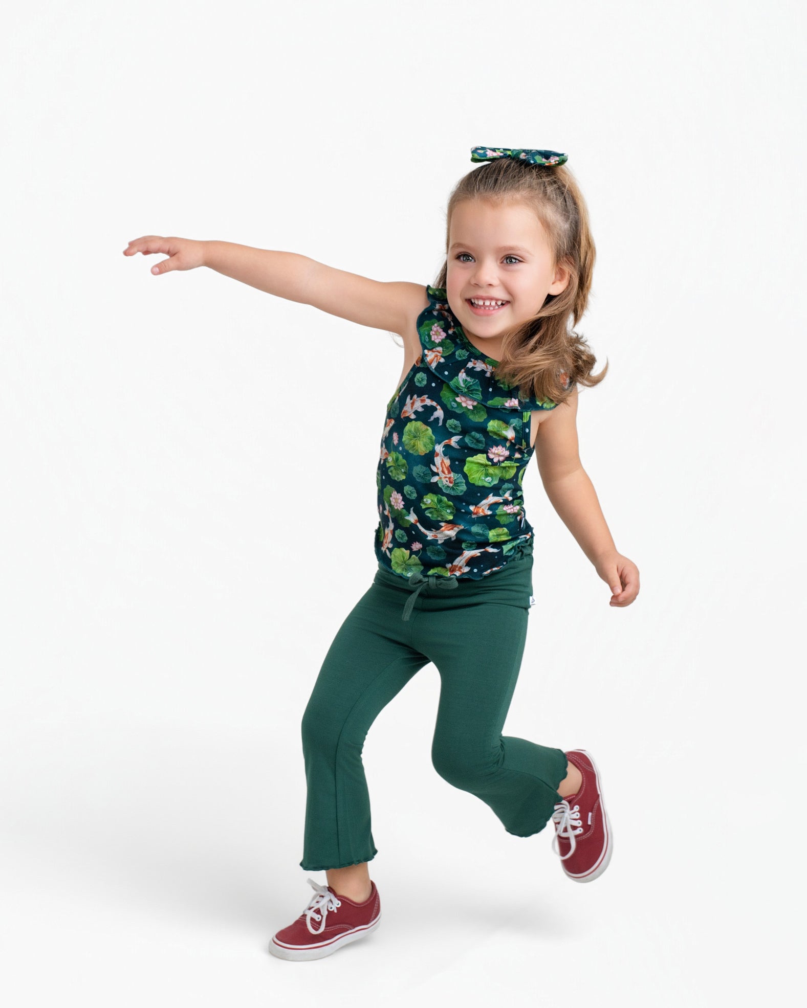 A young child poses playfully in the Jammie Session Bundle of Koi Bloomy Crop Set, featuring a green floral top and matching pants, against a plain white background.