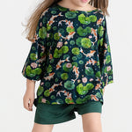 A child models the Jammie Session Bundle of Koi Comfy Cloud Short Set, featuring a dark shirt with a koi fish and lily pad print and matching dark green shorts, against a plain light background.