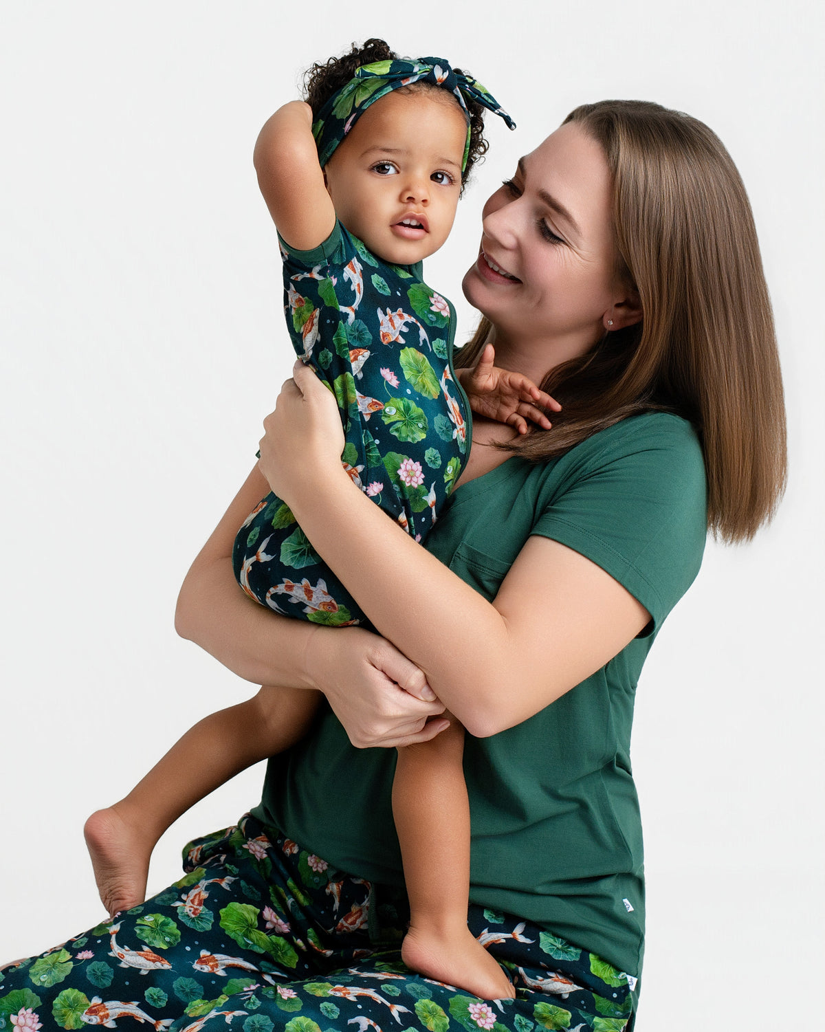 A woman smiles while holding a toddler, both wearing matching Jammie Session Bundle of Koi Women's Solid Short Sleeve T-shirts, combining comfort and style against a plain white background.