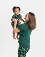 A woman in a green Jammie Session Bundle of Koi Women's Solid Short Sleeve T-shirt lifts a smiling toddler in matching pajamas against a plain white background.