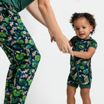 An adult and toddler stand against a white background, holding hands in matching Jammie Session dark green outfits with koi fish and lily pads; the toddler wears the Bundle of Koi Short Sleeve Romper.