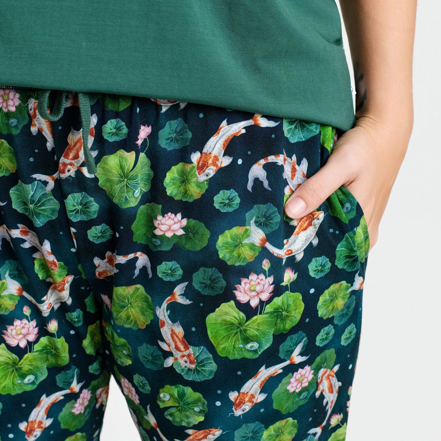 A person wearing Jammie Session's Bundle of Koi Women's Jogger Pants, featuring a vibrant koi fish and lotus flower design, with one hand casually in the pocket.