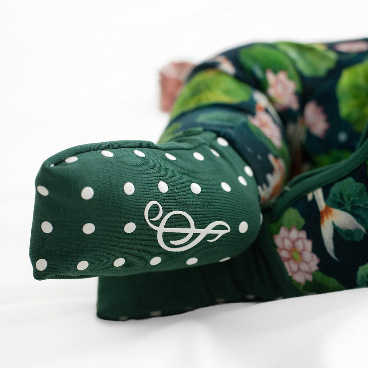 Close-up of a green polka-dotted padded accent with a white symbol on the Bundle of Koi Romper by Jammie Session, featuring a floral pattern and convertible footed design, displayed on a white surface.