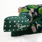 Close-up of a green polka-dotted padded accent with a white symbol on the Bundle of Koi Romper by Jammie Session, featuring a floral pattern and convertible footed design, displayed on a white surface.