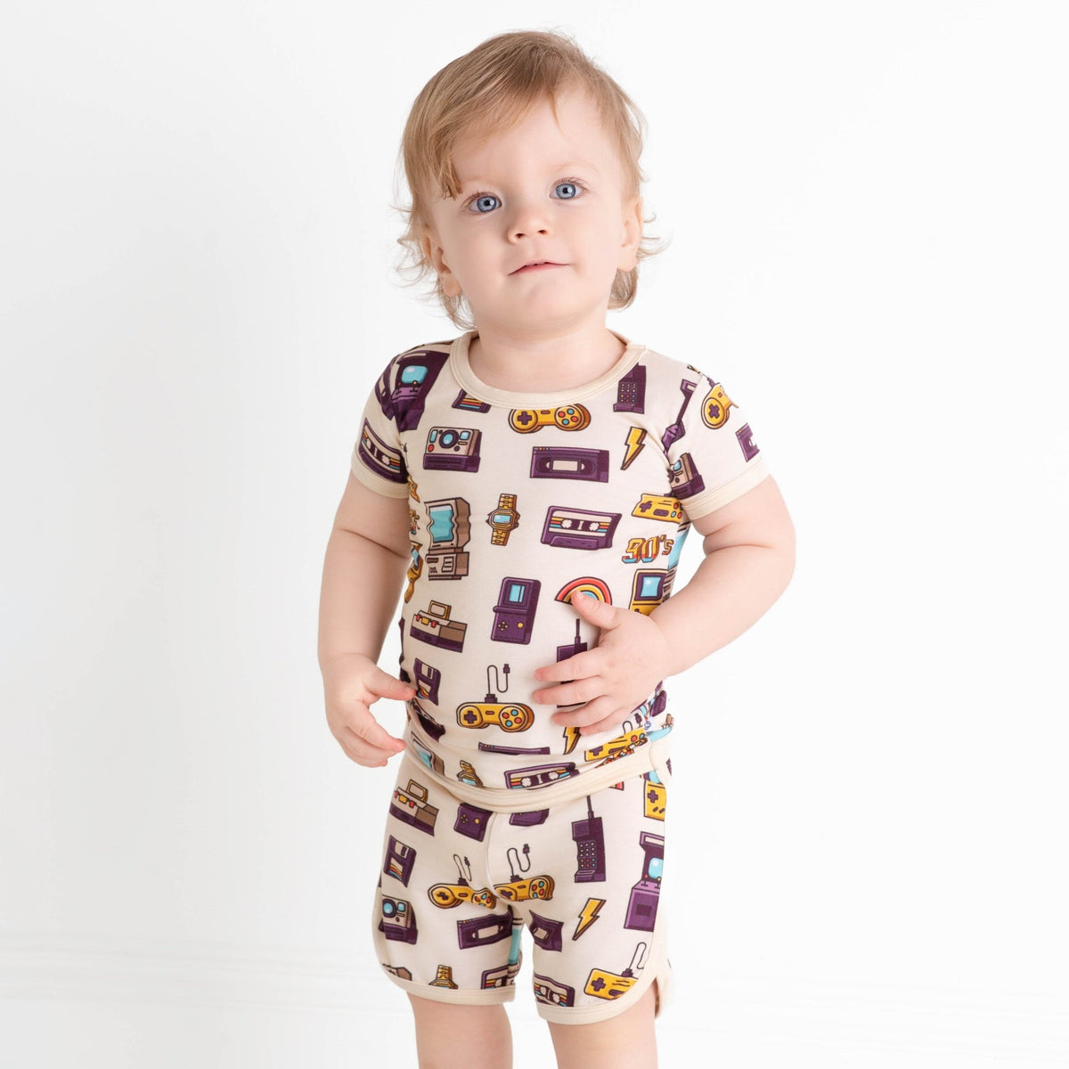 A toddler with light hair stands against a white background, wearing the Jammie Session 90's Retro Short Pajama Set made from breathable, hypoallergenic bamboo fabric.