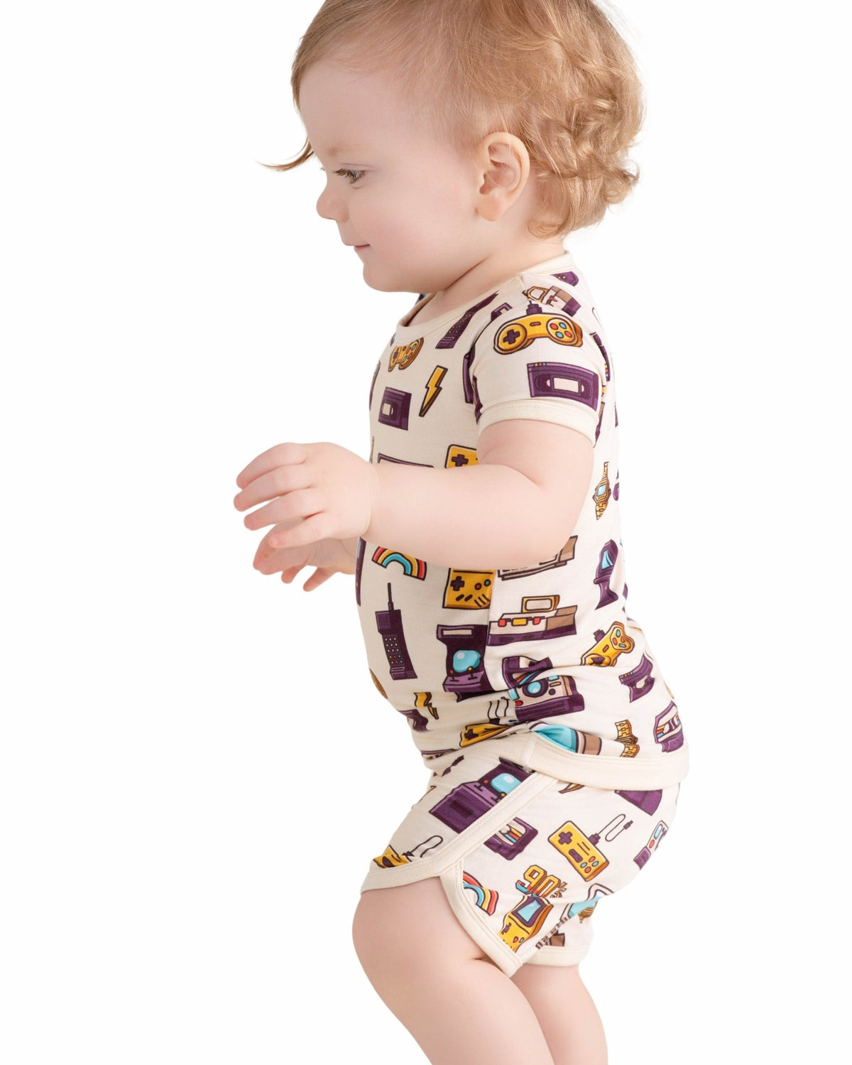A toddler stands against a plain white background wearing the Jammie Session 90's Retro Short Pajama Set—breathable, hypoallergenic bamboo baby clothes featuring colorful retro prints with matching short sleeves and shorts.