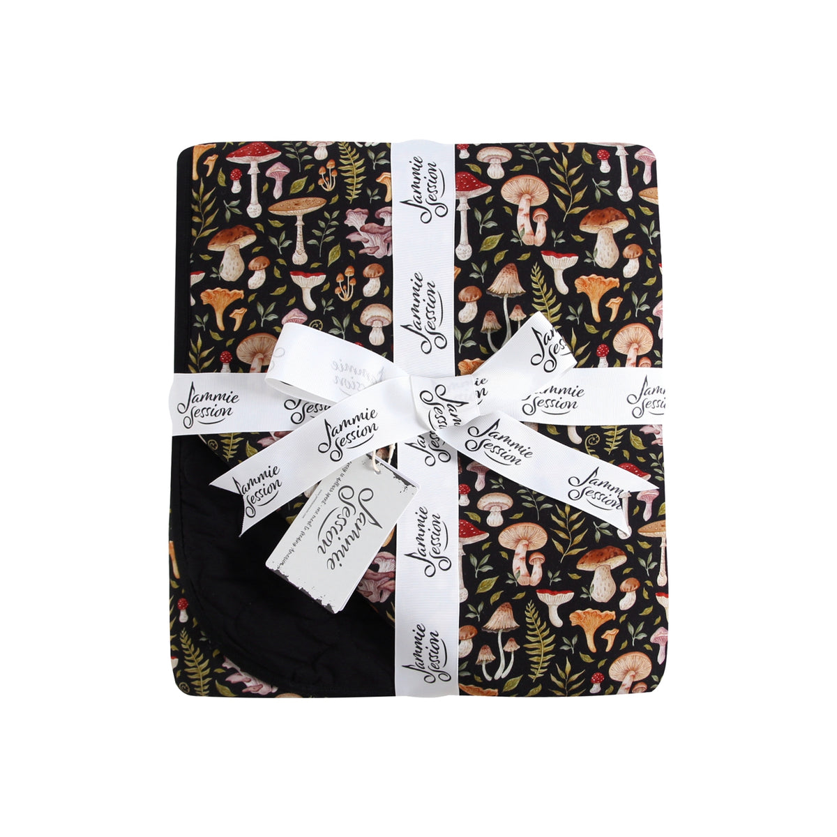 The Mystic Mushrooms Adult Quilted Blanket by Jammie Session is a folded black bamboo blanket with a vibrant mushroom and foliage pattern, tied with a white "Jammie Session" ribbon for breathable comfort and stylish coziness.