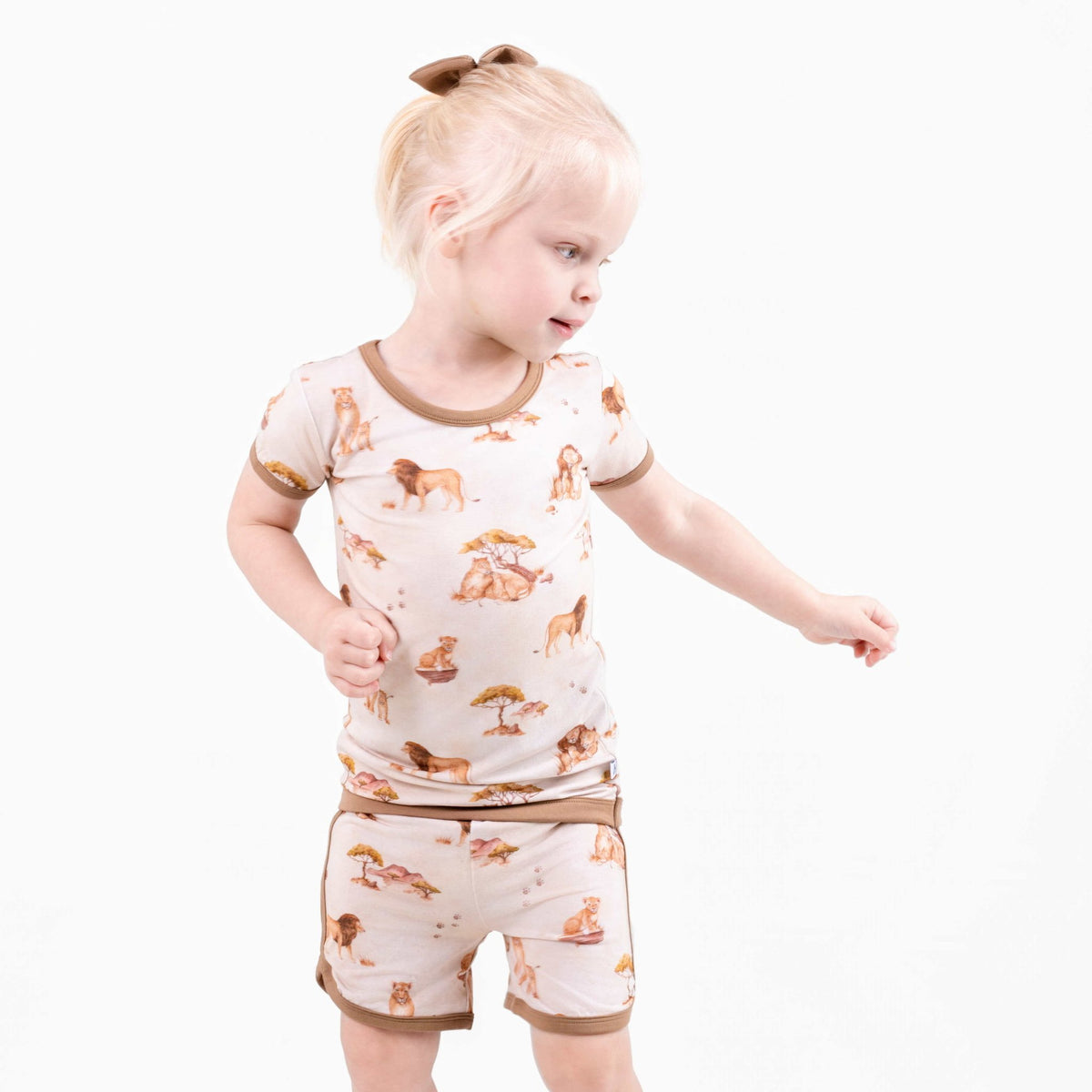 A young child with blonde hair in a ponytail wears the Ari (Lion) TENCEL™ Modal Short Pajama Set by Jammie Session, crafted from buttery soft, hypoallergenic fabric, standing against a plain white background.