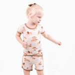 A young child with blonde hair in a ponytail wears the Ari (Lion) TENCEL™ Modal Short Pajama Set by Jammie Session, crafted from buttery soft, hypoallergenic fabric, standing against a plain white background.