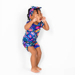 A young child models the Jammie Session Cosmic Cuddles Zodiac Short Pajama Set with a matching headband, standing barefoot and playfully posing against a plain white background.