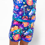 A child wears the Jammie Session Cosmic Cuddles Zodiac Short Pajama Set, crafted from buttery soft, hypoallergenic bamboo and adorned with lions, crabs, unicorns, and stars on a dark blue background.