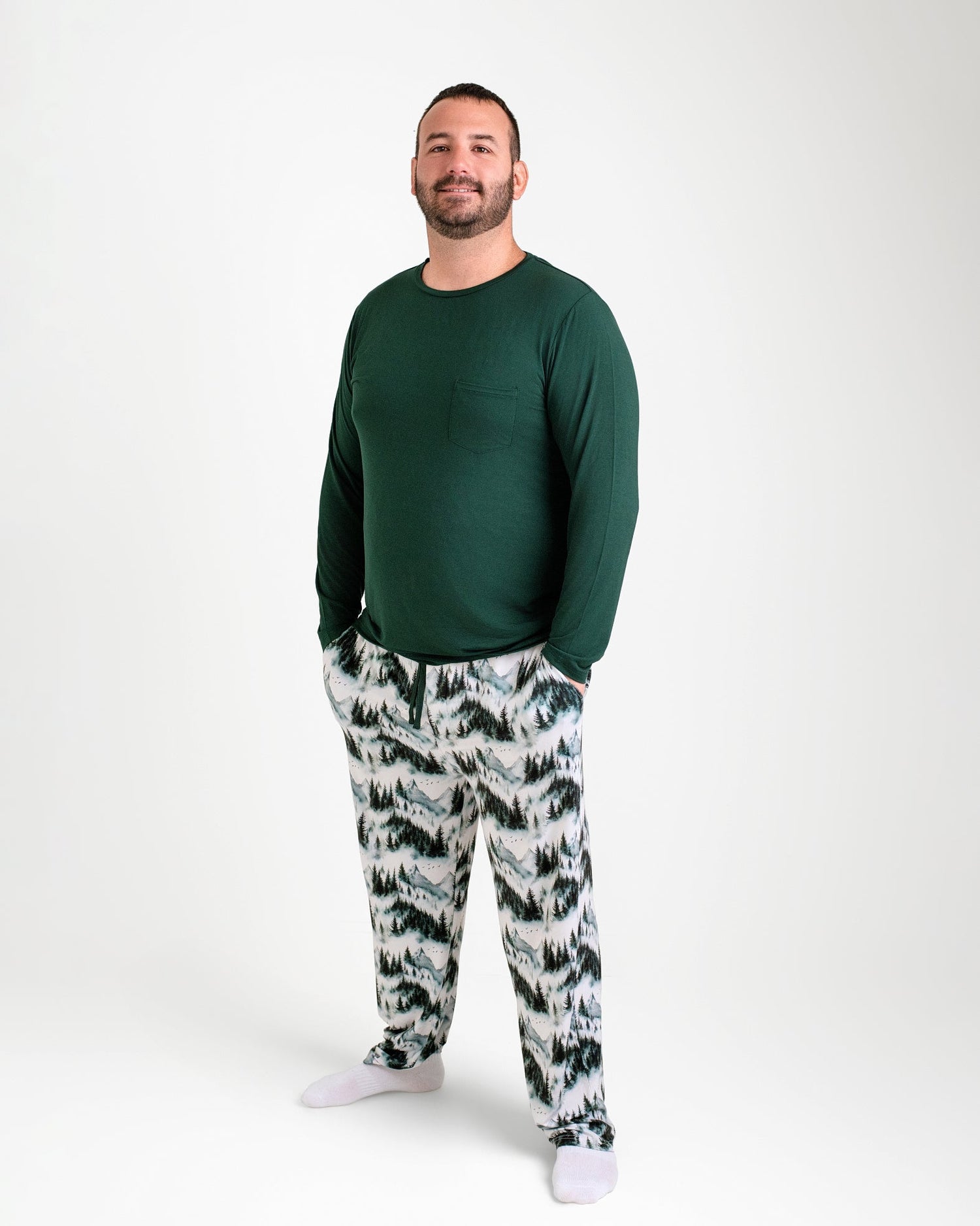 A man faces forward in Jammie Session Mountain Mist Men's PJ Pants, paired with a soft dark green long-sleeve shirt and white socks, all against a plain white background.