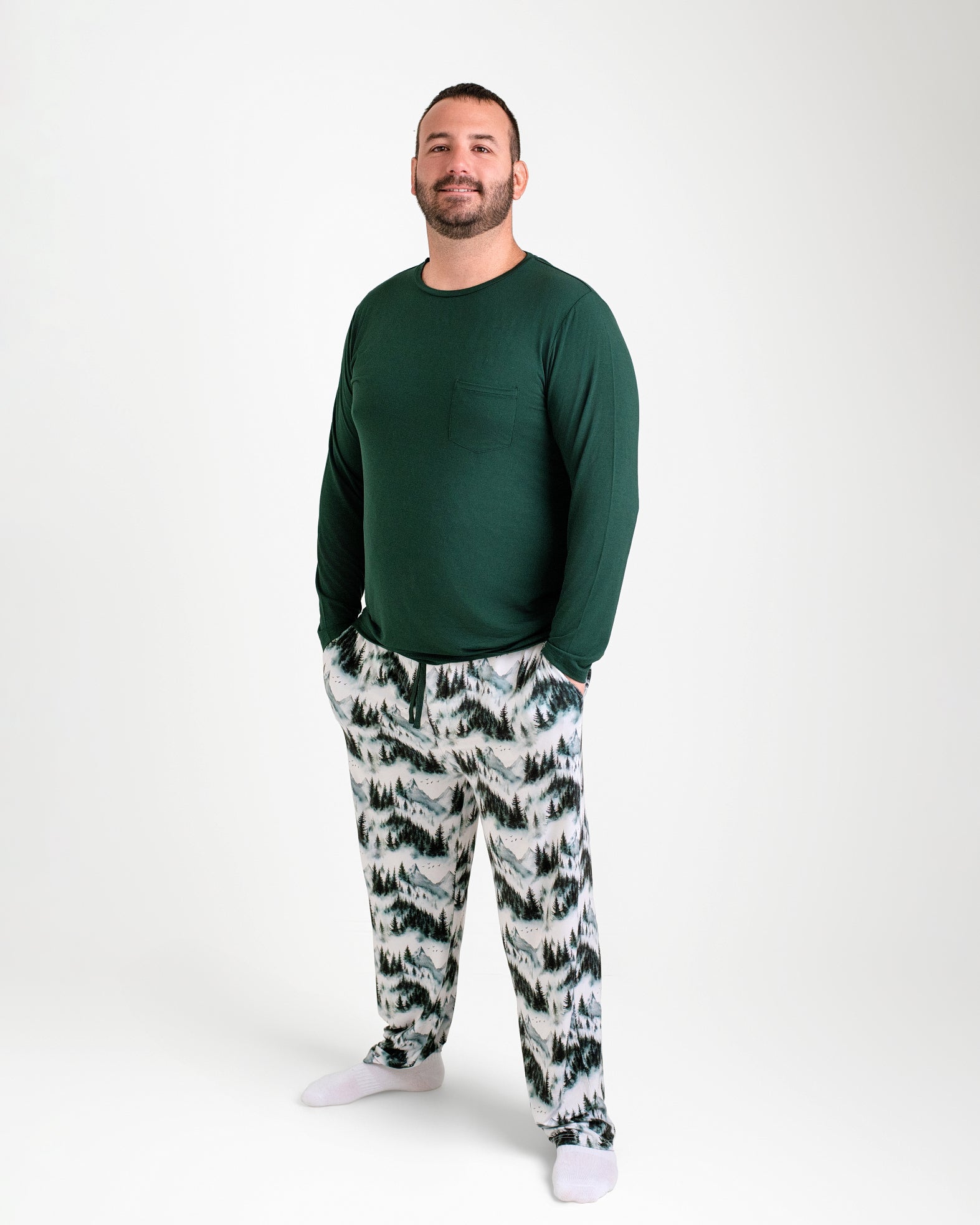 A man faces forward in Jammie Session Mountain Mist Men's PJ Pants, paired with a soft dark green long-sleeve shirt and white socks, all against a plain white background.