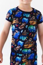 A child wears the Jammie Session Nocturnal Nonsense Short Pajama Set, which features a colorful raccoon and garbage print on navy blue. This hypoallergenic, breathable set keeps kids comfy and stylish all day.