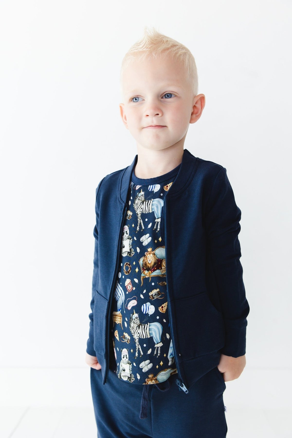 A young child with short blonde hair wears the Jammie Session Up Zoo Late Solid Kids' Jacket (runs small, please size up) and matching pants, paired with an animal print shirt, standing against a plain white background.