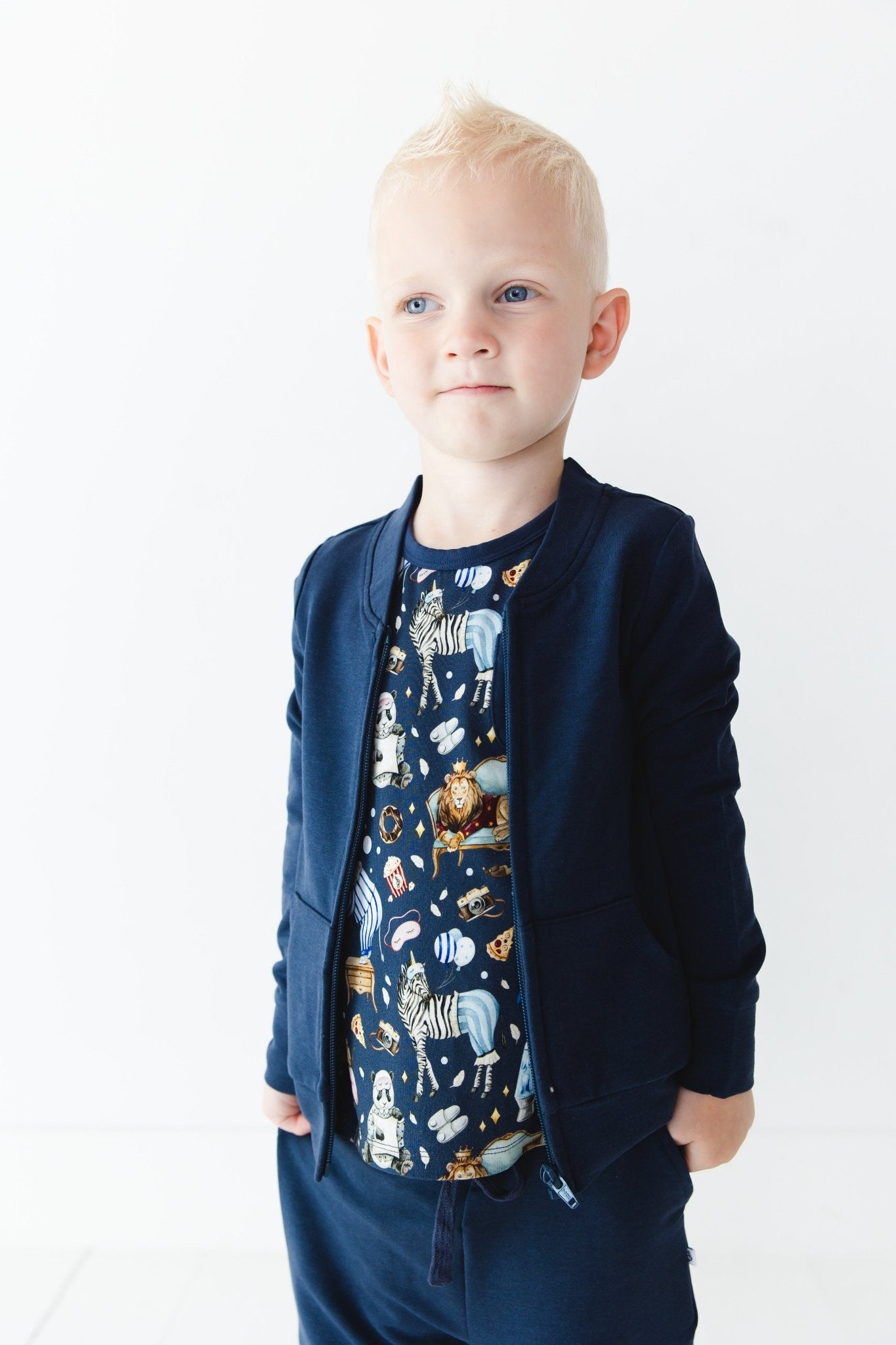 A young child with short blonde hair wears the Jammie Session Up Zoo Late Solid Kids' Jacket (runs small, please size up) and matching pants, paired with an animal print shirt, standing against a plain white background.