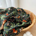 Load image into Gallery viewer, A wicker basket holds the Jammie Session "Wood You Be My Friend" breathable and cozy bamboo cotton muslin swaddle blanket, featuring woodland animal and foliage patterns, placed on a wooden surface next to cotton.
